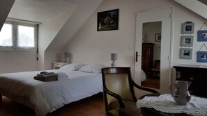 Ein Schlafzimmer mit einem Bett, einem Sessel, einem Nachttisch, einer Lampe, einem Bild an der Wand und einer Tür zu einem anderen Raum.