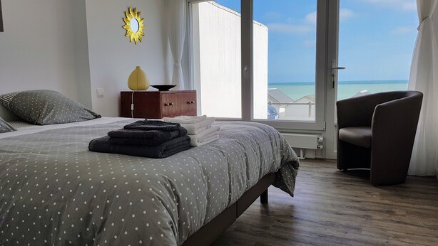 A bedroom with a bed, a chair, a dresser, and a view of the sea.