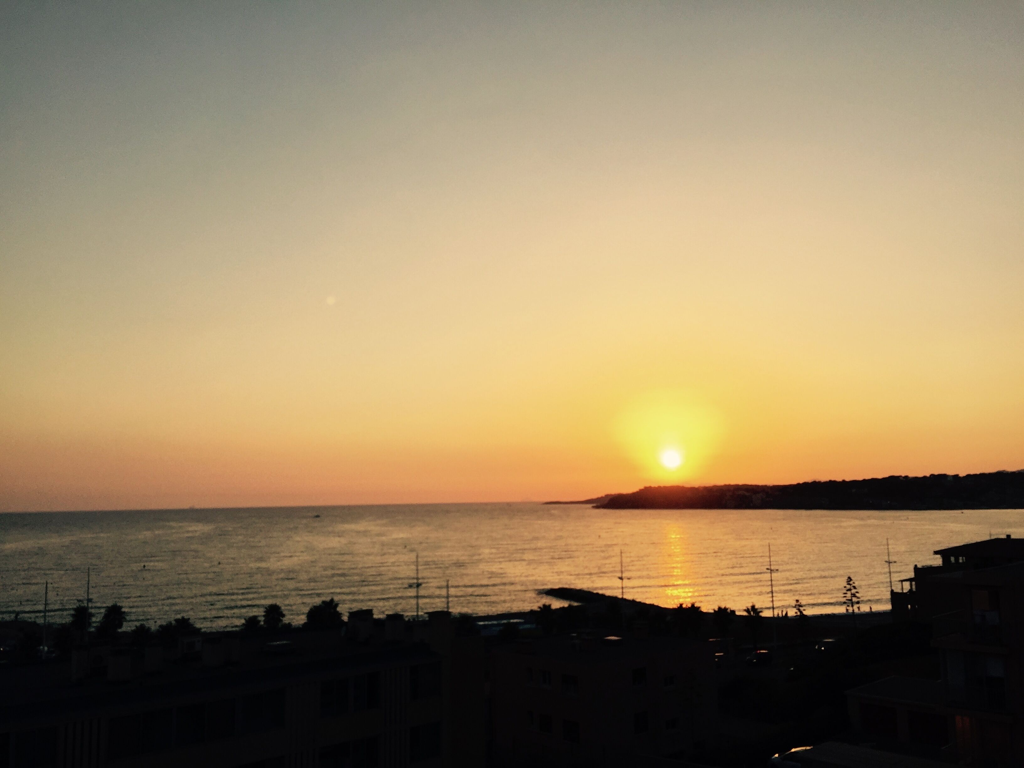 A coastal sunset with silhouettes of buildings and a clear sky.