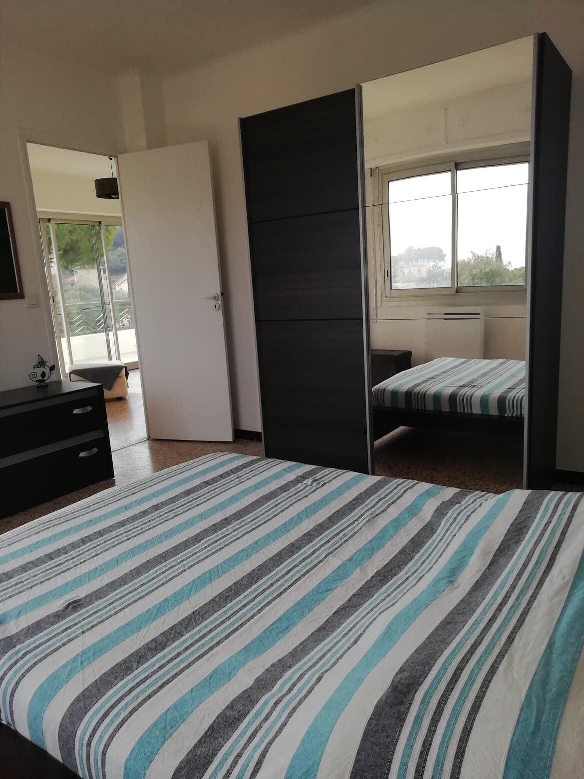 Une chambre à coucher comprenant un lit, une commode, une fenêtre et une porte coulissante donnant sur un balcon.