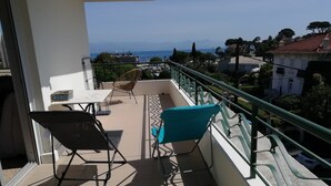 Een balkon met twee stoelen, een tafel en uitzicht op zee en bergen.