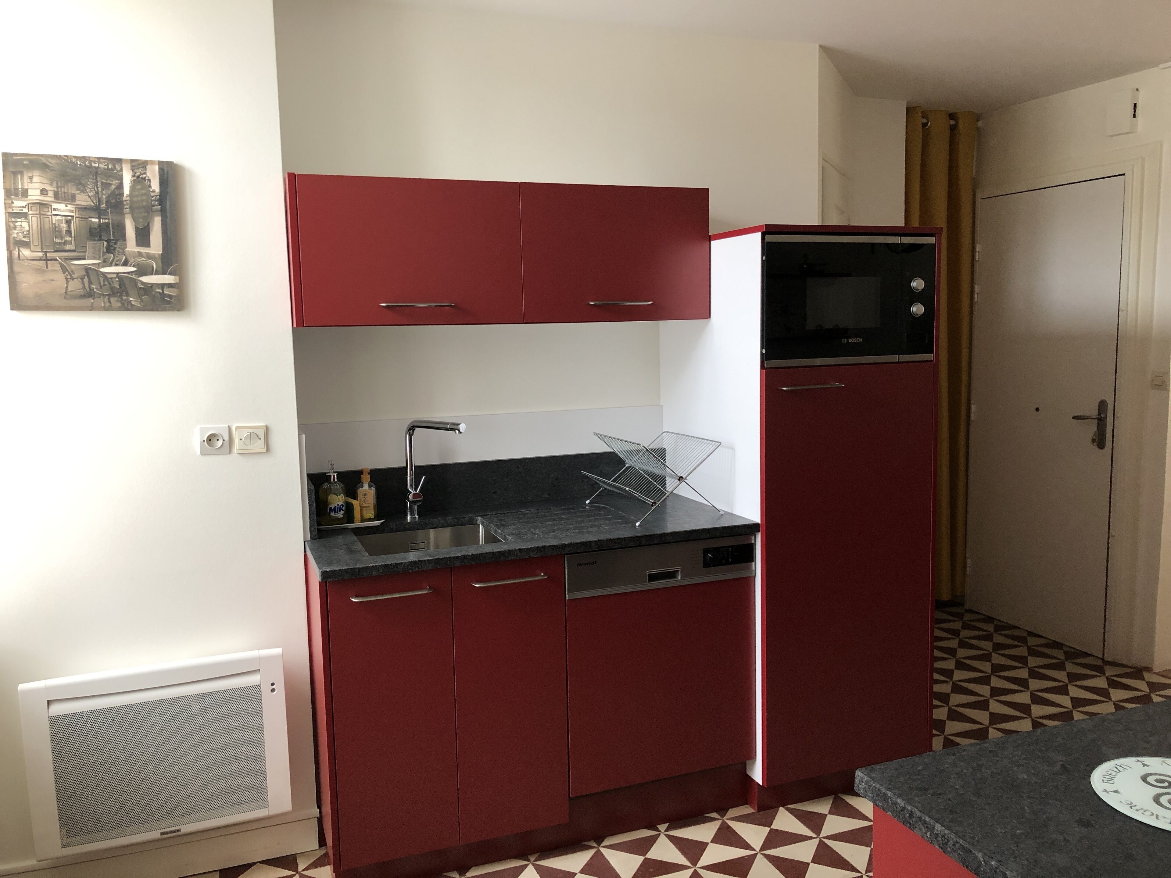 A compact kitchen with red cabinets, a black countertop, and a Bosch microwave.