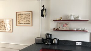 Una cocina con armarios rojos, una cafetera y un tostador. Hay dos láminas botánicas enmarcadas en la pared.