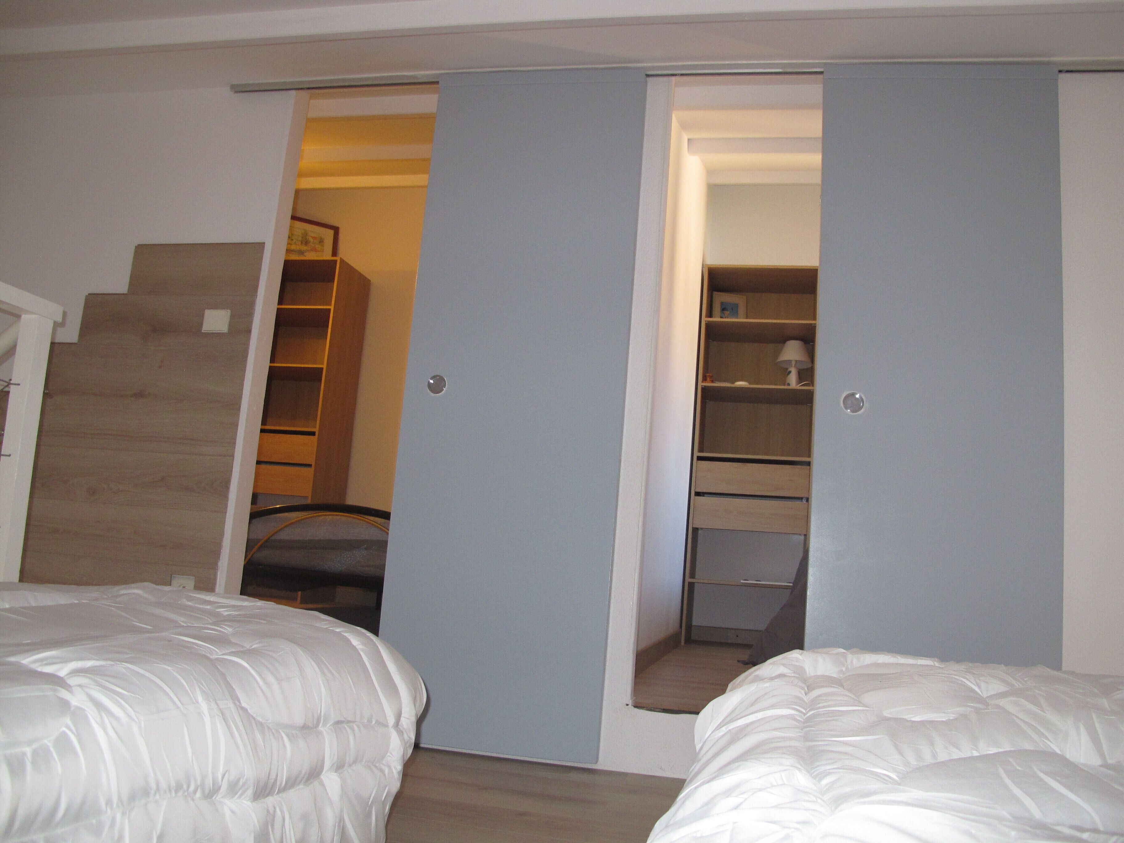 Une chambre avec deux lits, un escalier en bois et une armoire avec des étagères.