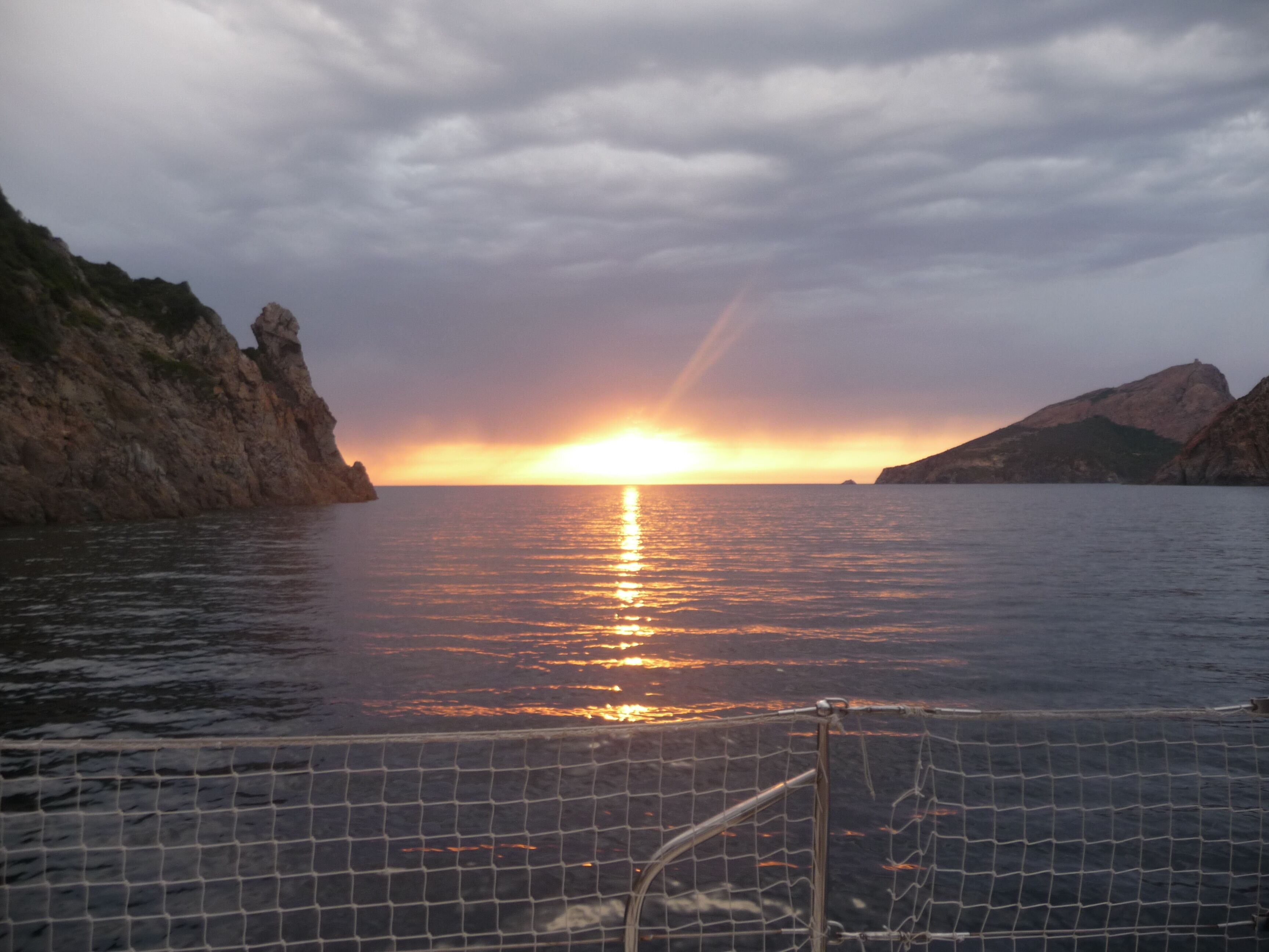 Un tram sol mentre el sol se submergeix en un cos d'aigua, flanquejat per penya-segades rocoses.
