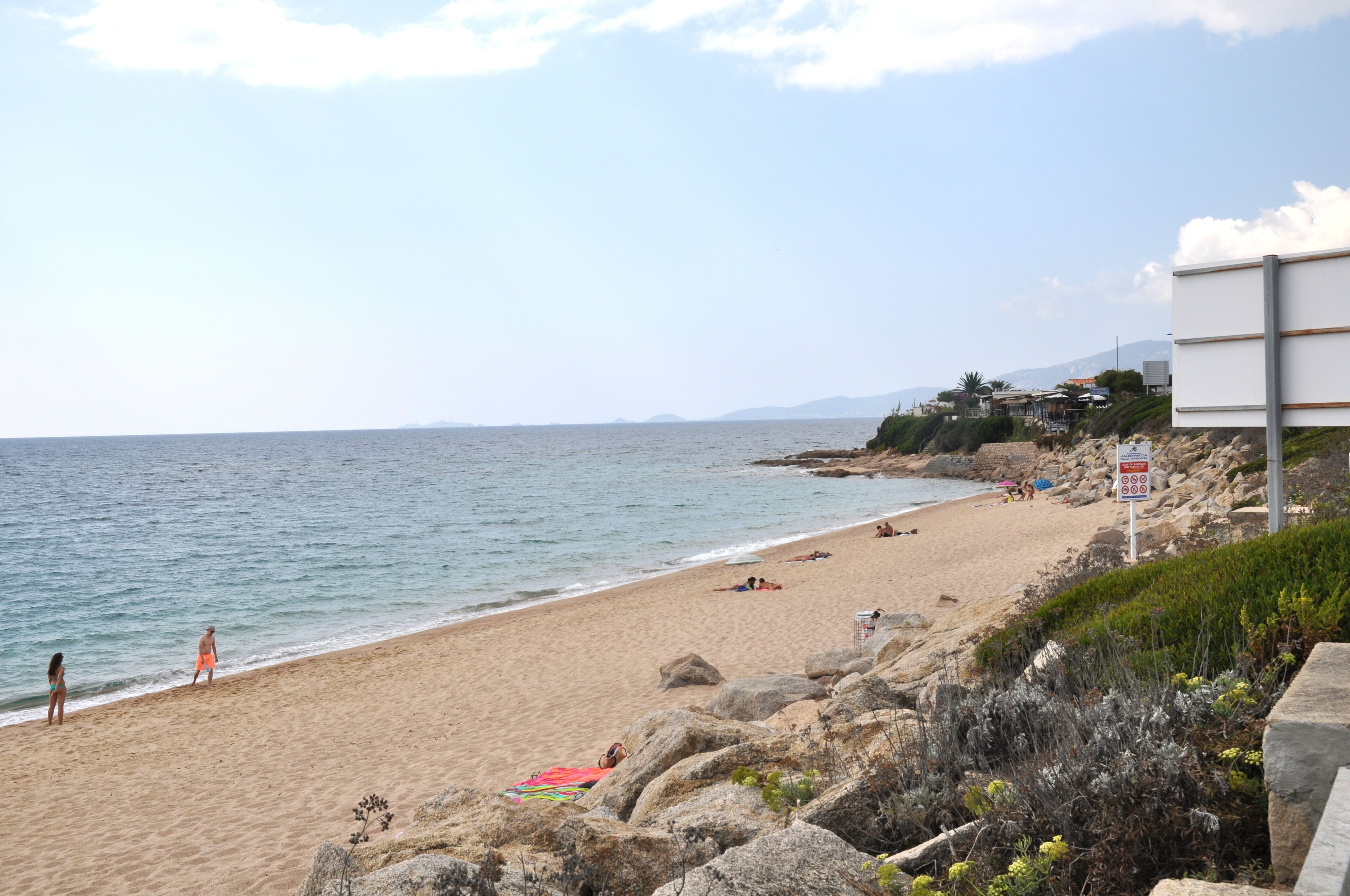 Une plage avec un terrain rocheux et quelques personnes.