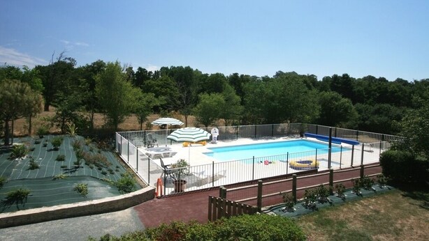Una piscina con un deck cercado, sillas de descanso y sombrillas.