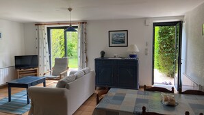 Una sala de estar con sofá, televisión, mesa con mantel, aparador y una silla.