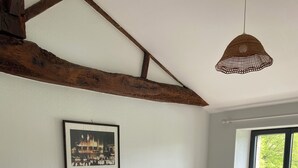 Una habitación con dos camas, vigas de madera en el techo, un cuadro en la pared y una ventana con vistas al verdor.