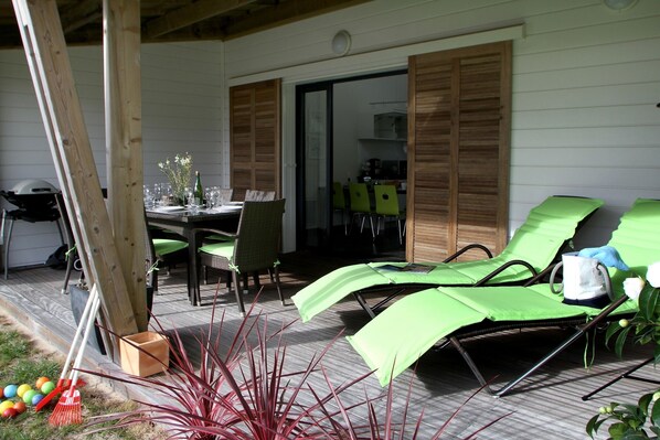 A patio with a table set for dining, green lounge chairs, and a wooden deck.