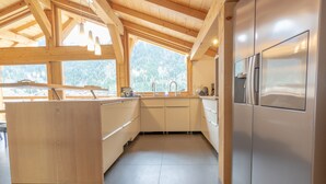 Een moderne keuken met houten balken, een groot eiland, roestvrijstalen apparatuur en uitzicht op het bos.