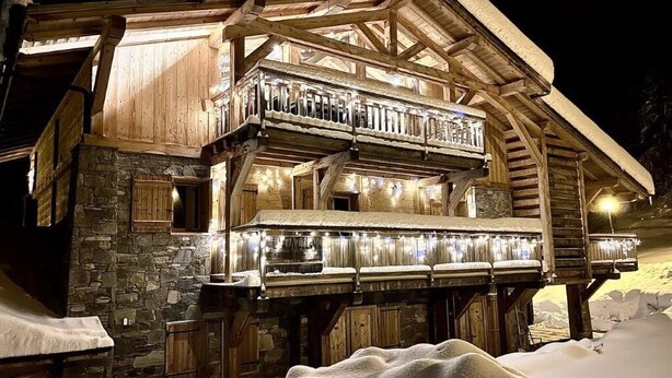 Een houten chalet met balkon, stenen muren en een sneeuwbedekte grond.