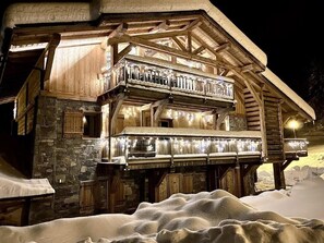 Un chalet en bois doté d’un balcon, de murs en pierre et entouré d’un paysage enneigé.