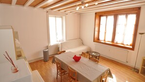 A room with a dining table, chairs, a sofa, and a window with curtains. - Apartment Prémanon town center 6p (Prémanon)