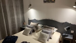 Un lit bien fait, agrémenté de plusieurs oreillers et d’une couverture, une lampe de chevet, une petite table avec une lampe et un cadre photo fixé au mur.