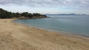 Une plage avec un rivage sablonneux, une eau calme et une chaîne de montagnes lointaine sous un ciel nuageux.