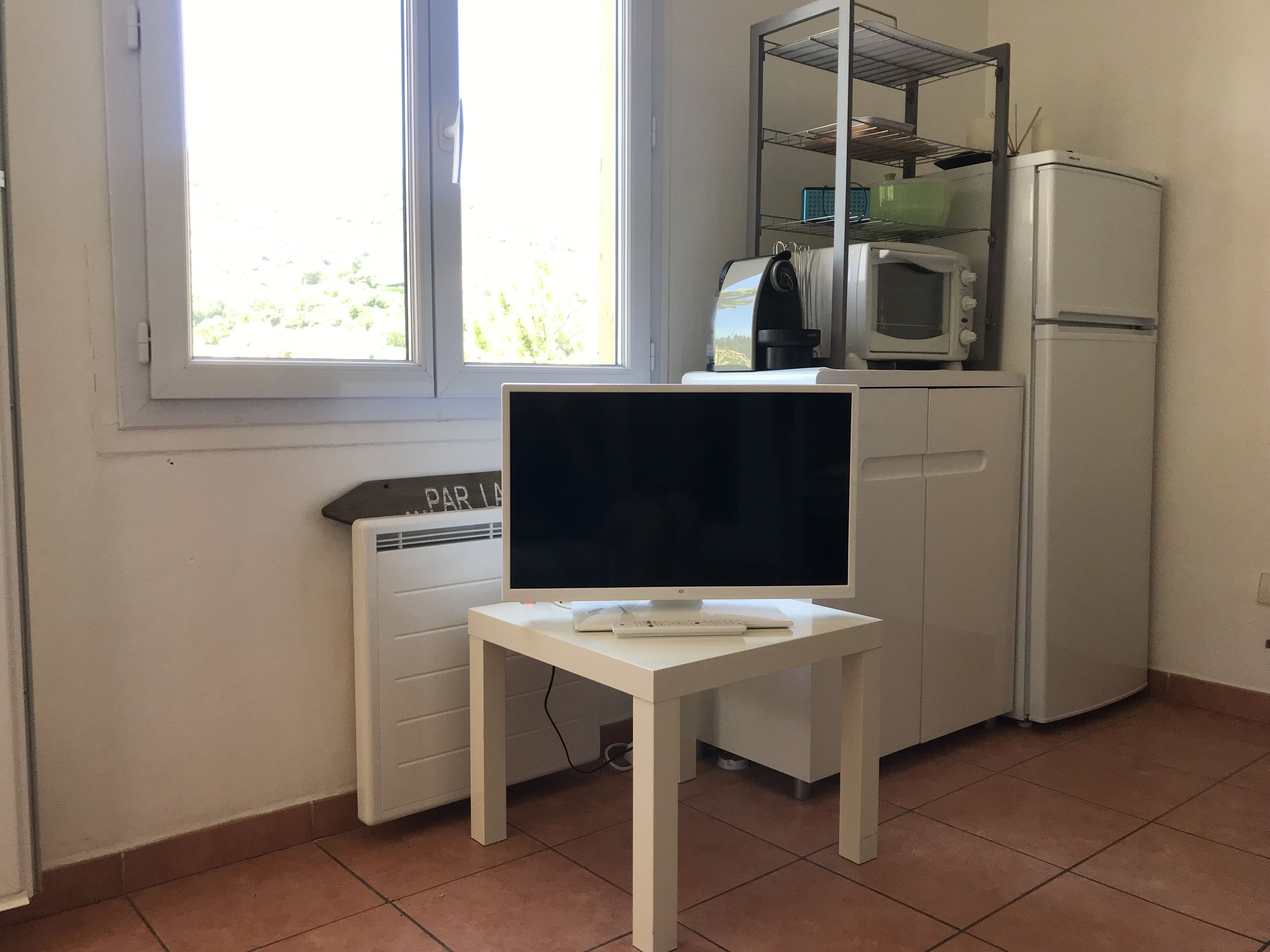A kitchen with a white refrigerator, a microwave, and a white table with a flat-screen TV.