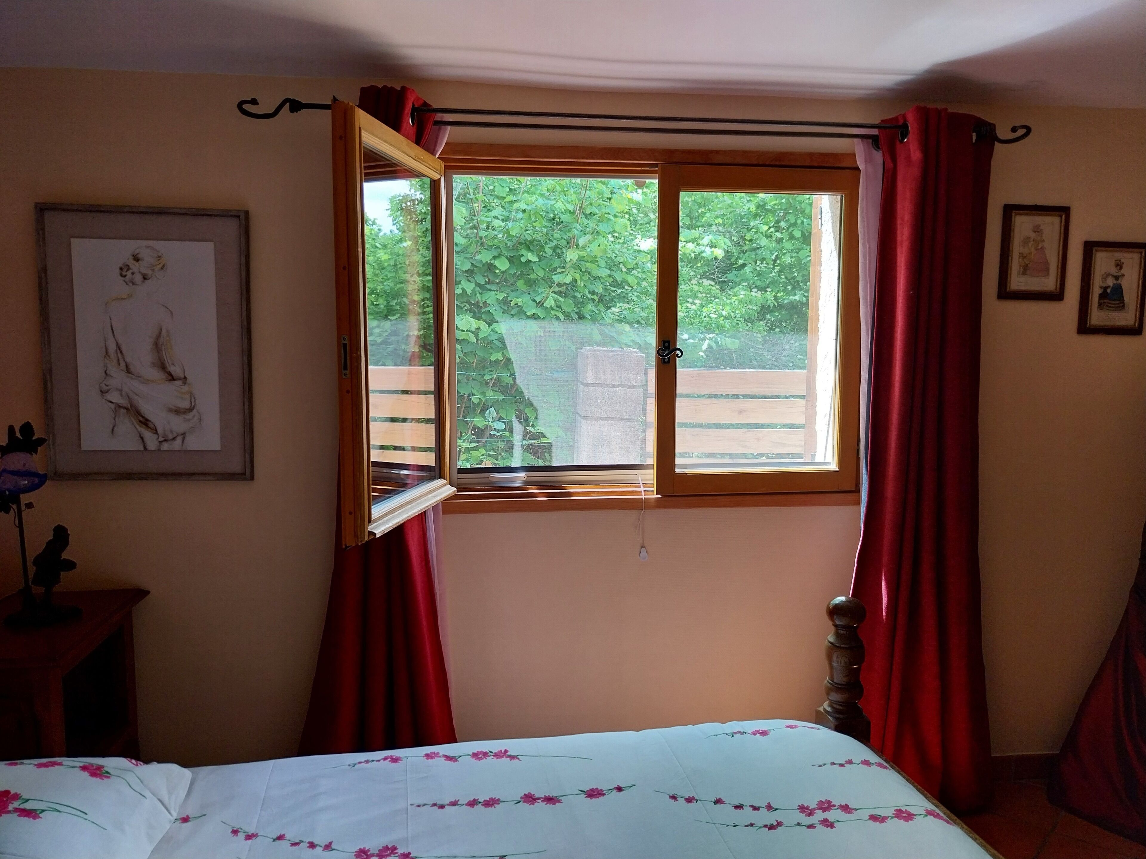 Un dormitorio con una cama, un ventanal con cortinas rojas y un cuadro en la pared.