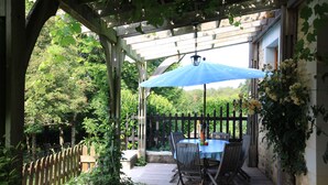 A wooden deck with a table and chairs under a pergola, surrounded by greenery. - Haven of peace, sweet home, swimming pool, 7 beds between Tours and Poitiers (Senillé-Saint-Sauveur)