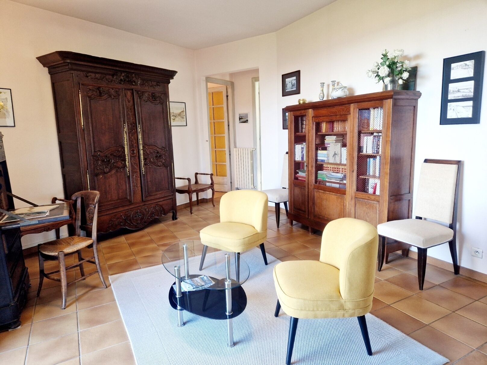 Una sala de estar con un mueble grande de madera, dos sillones amarillos, una mesa de centro de vidrio y una estantería.