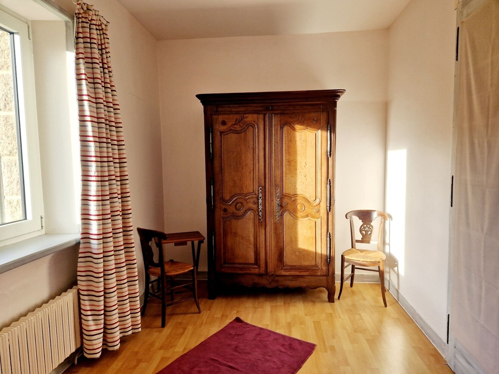 Habitació amb armari de fusta, una cadira, taula petita i radiador.