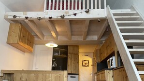 A compact kitchen with wooden cabinets, a small refrigerator, and a staircase leading to an upper level. - Avoriaz center, Large  Studio on two levels:rented from Saturday to Saturday  (Morzine)