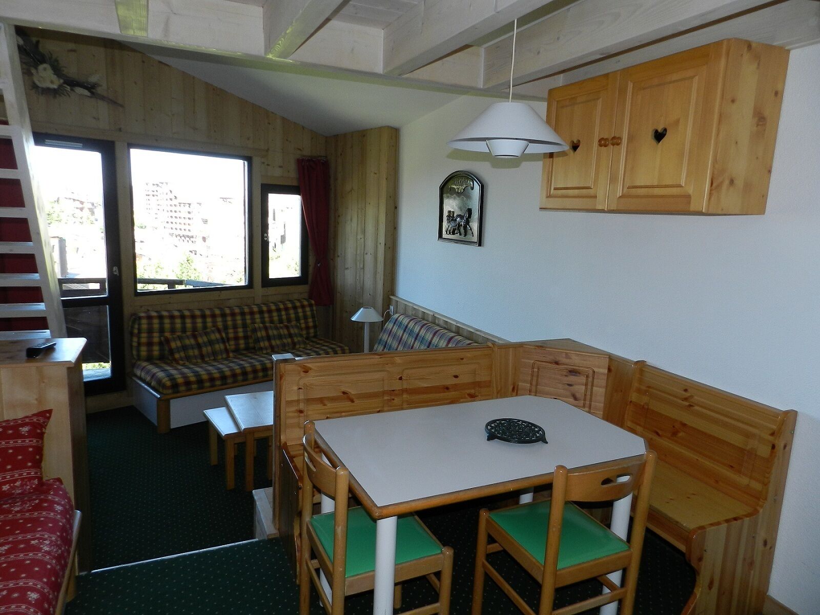 Ein gemütliches Blockhaushaus-Interieur mit einem Holzesstisch, grünen gepolsterten Stühlen, einer Bank und einem Sofa.