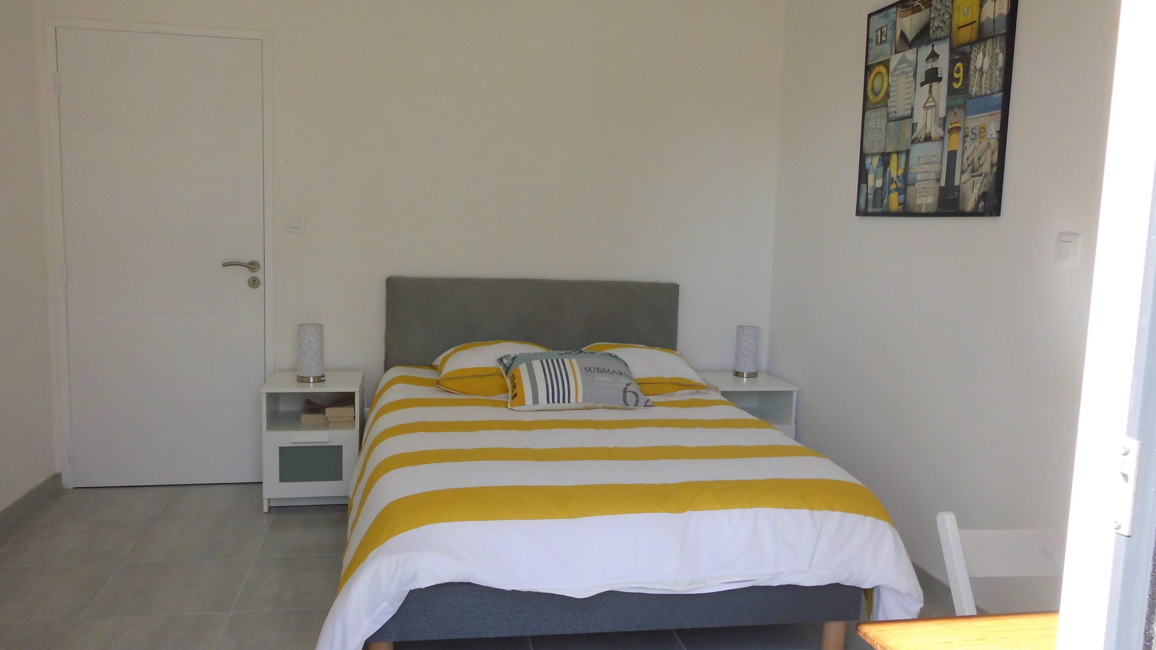 A bedroom with a bed, two bedside tables, a door, and a wall art piece.