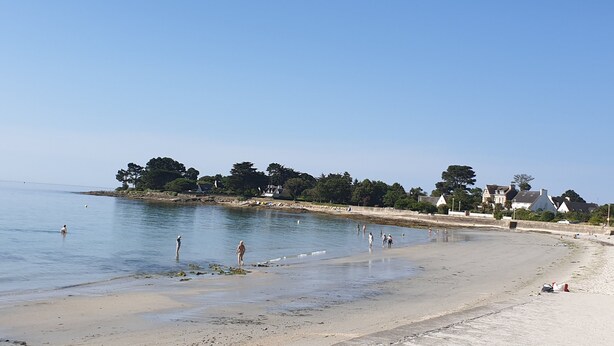 Une plage aux eaux calmes, avec un rivage sablonneux et des bâtiments en arrière-plan.
