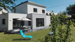 Une maison moderne à deux étages dotée d’un patio aménagé avec des meubles d’extérieur et un fauteuil bleu.