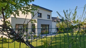 Une maison moderne à deux étages, dotée d’un toit plat, de grandes fenêtres et d’un balcon apparent.