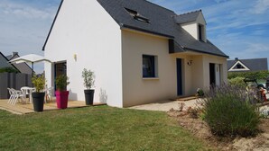 A modern house with a sloped roof, a patio with outdoor furniture, and potted plants. - 3-star seaside villa, sleeps 7, 150 m from the beach and the GR34 trail. Large, enclosed garden (Plounéour-Brignogan-Plages)