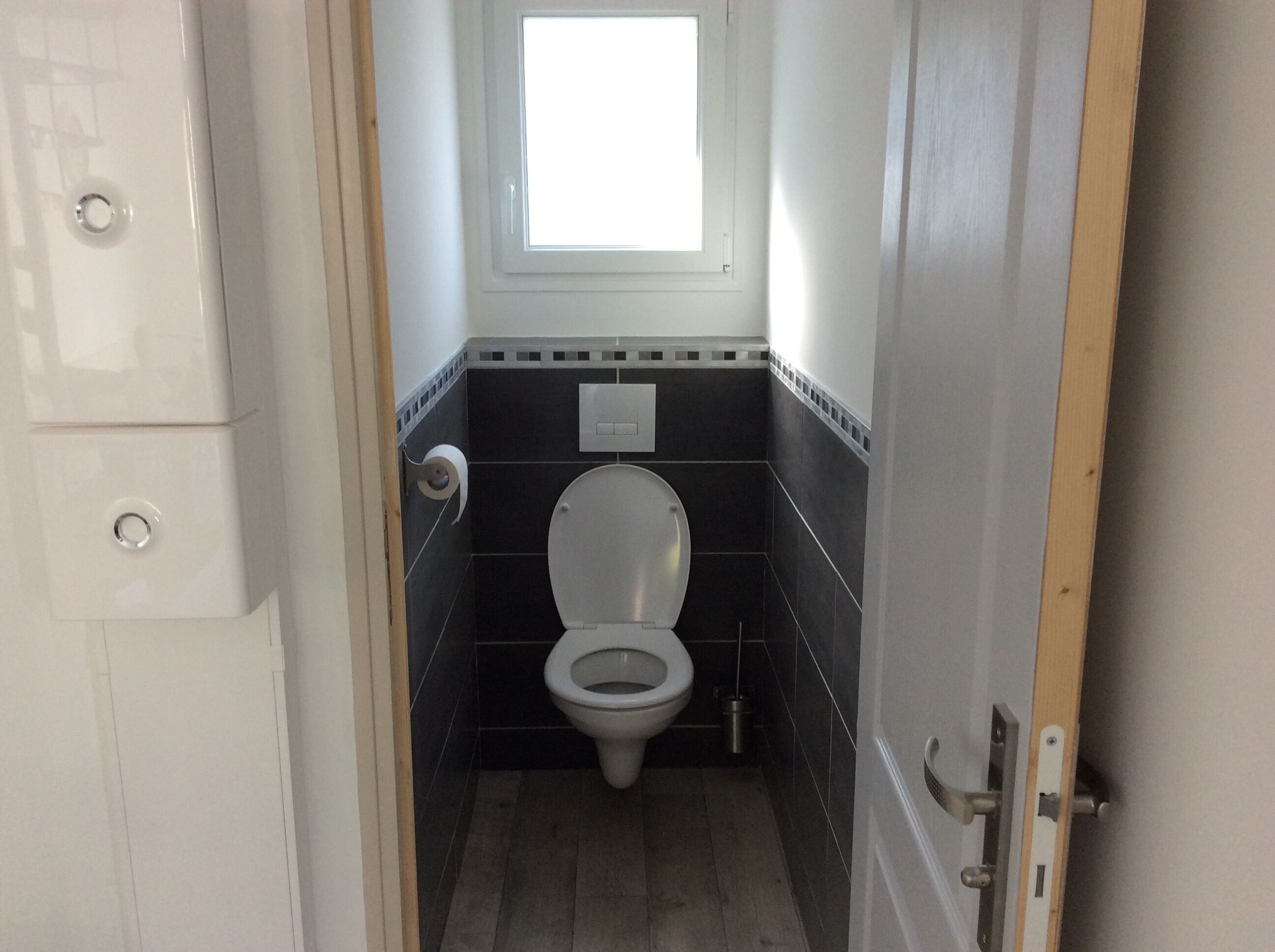 Een kleine badkamer met toilet, raam en een zeepdispenser.