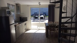 A compact kitchen with a refrigerator, microwave, and sink. There is a dining area with a table and chairs, and a staircase leading to an upper level.