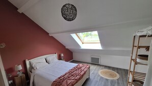 A bedroom with a sloped ceiling, a skylight, a bed with white linens, a pink throw blanket, a bedside table with a lamp, a wooden ladder, and a woven rug.