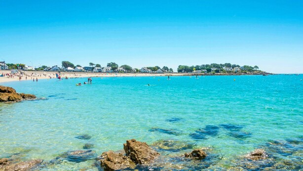 A beach with clear turquoise water, rocky shoreline, and a distant shoreline with buildings and trees. - The forest, 400 m from an arm of the sea.  (Carnac)