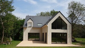 A modern house with a sloped roof, large glass windows, and a wooden deck. - The forest, 400 m from an arm of the sea.  (Carnac)