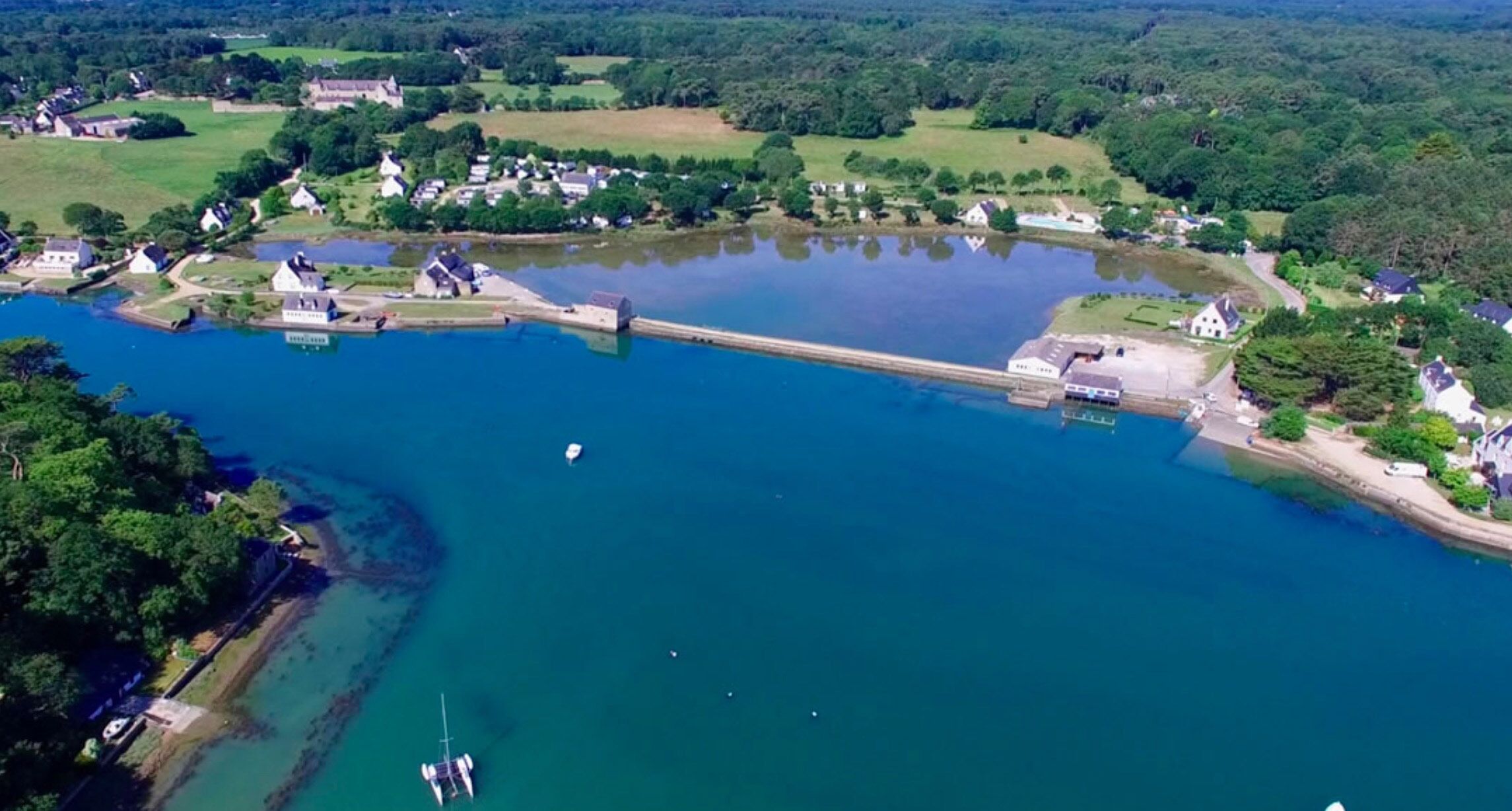 Luchtbeeld van een meer met een dam, omringd door woongebouwen en groen.