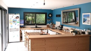 A kitchen with a wooden island, a refrigerator, a window with a view of greenery, and a clock on the wall. - The forest, 400 m from an arm of the sea.  (Carnac)