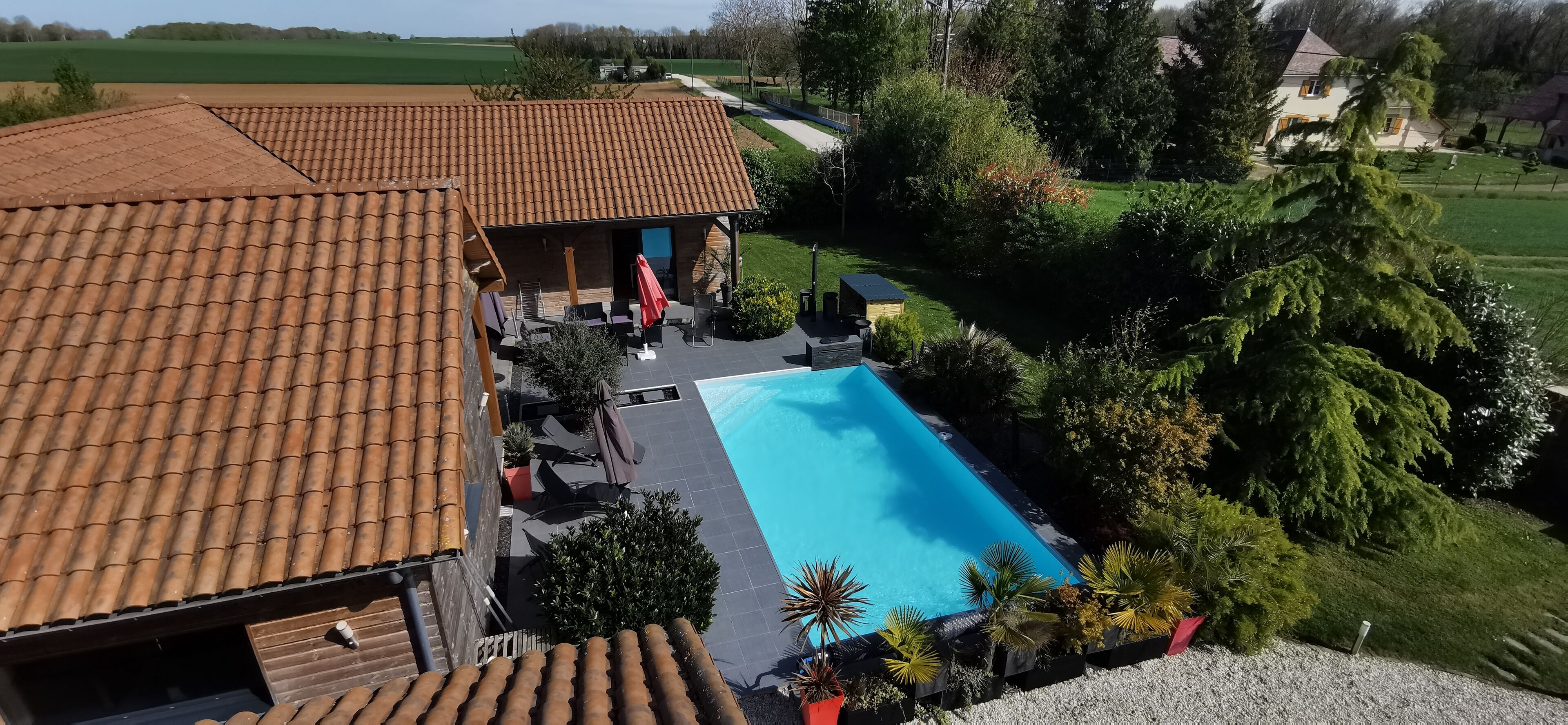 A house with a tiled roof, a swimming pool, and a garden with various plants.