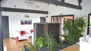 A modern living room with a white sofa, red cushions, a large plant, and a glass partition. - Vacation villa with swimming pool near Orient lakes in Champagne (Villa Temple) (Lesmont)