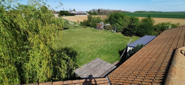 A view of a green lawn with a wooden deck and a brick roof.