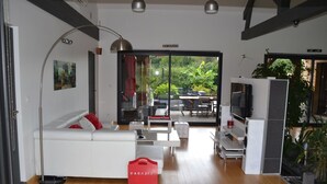 A modern living room with a white sofa, a coffee table, a TV, and a sliding glass door leading to an outdoor patio. - Vacation villa with swimming pool near Orient lakes in Champagne (Villa Temple) (Lesmont)