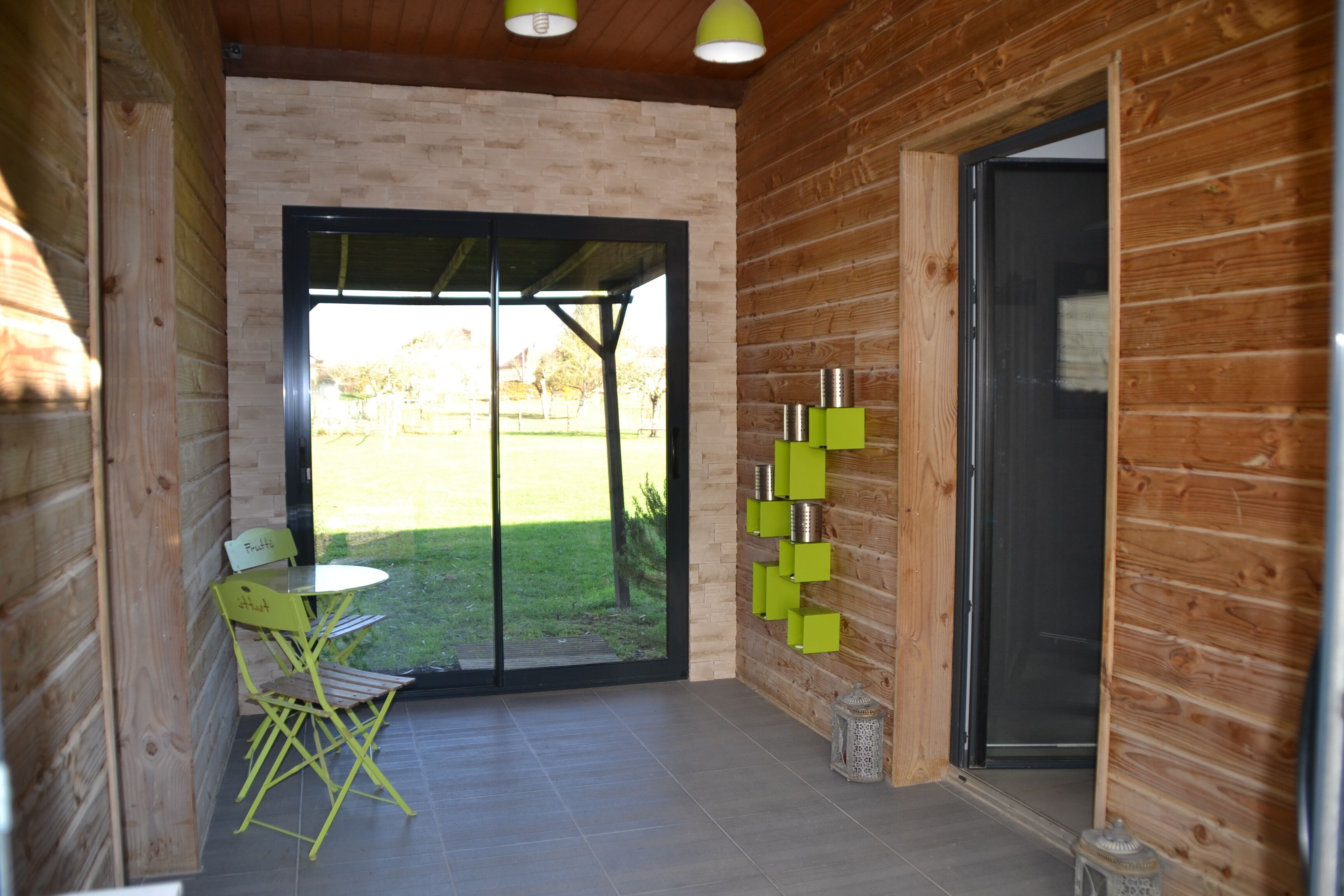 A modern log cabin interior with a dining area, a sliding glass door leading to a grassy yard, and a small outdoor seating area.