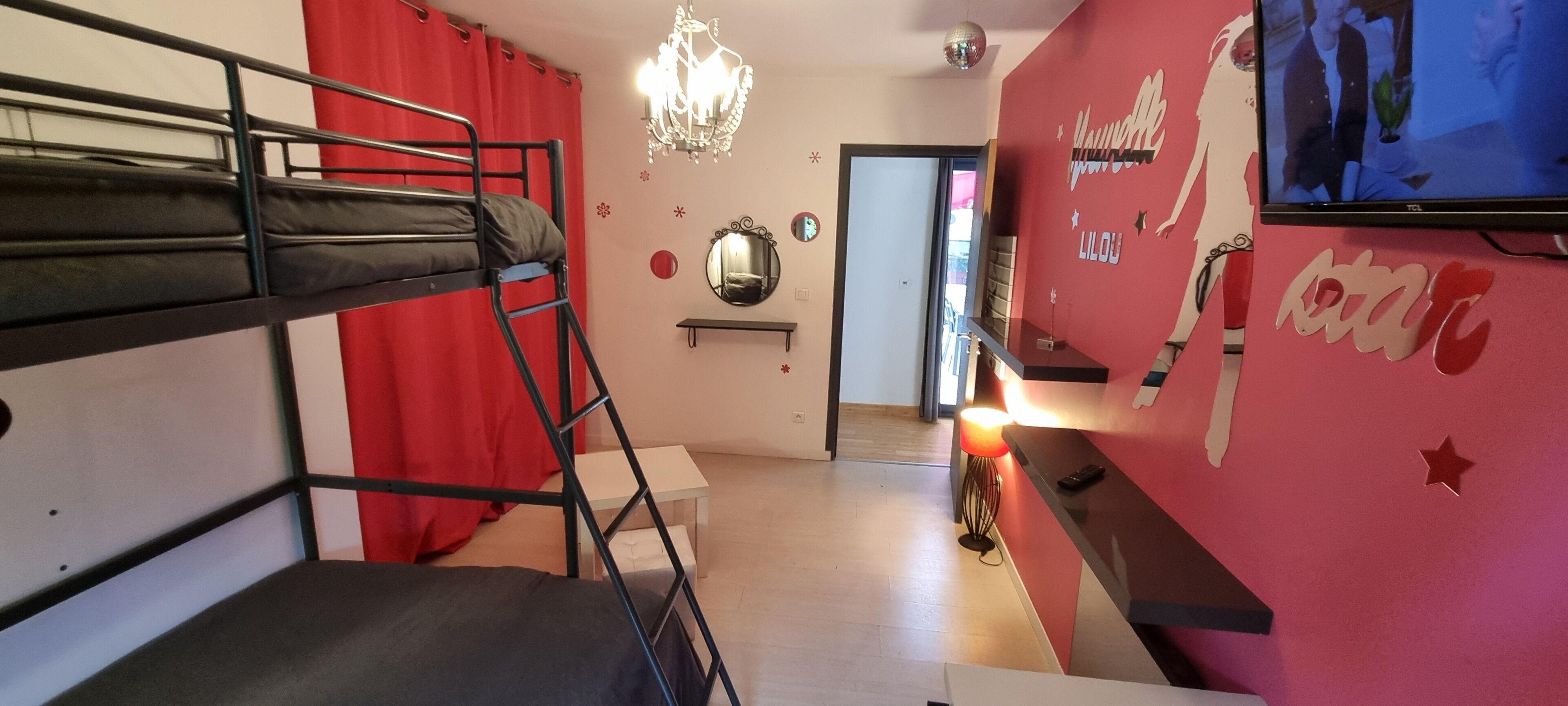 A bunk bed room with a red curtain, a chandelier, a mirror, and a TV on the wall.