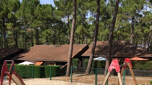 A playground with swings and slides, surrounded by a fence and trees. - Cottage in the heart of the pines (Lacanau Océan)