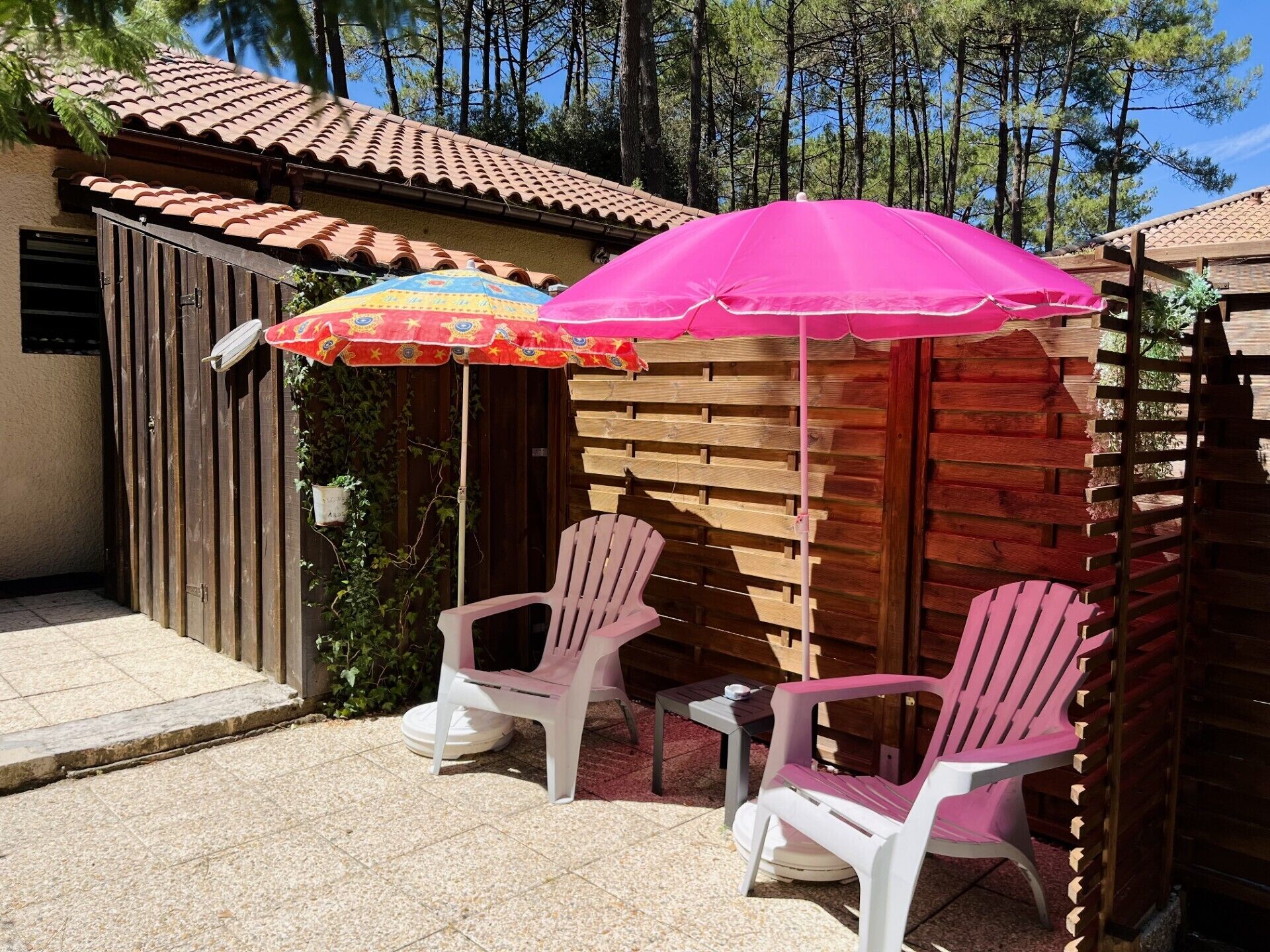 Une terrasse avec deux chaises en plastique blanches et un parasol rose.