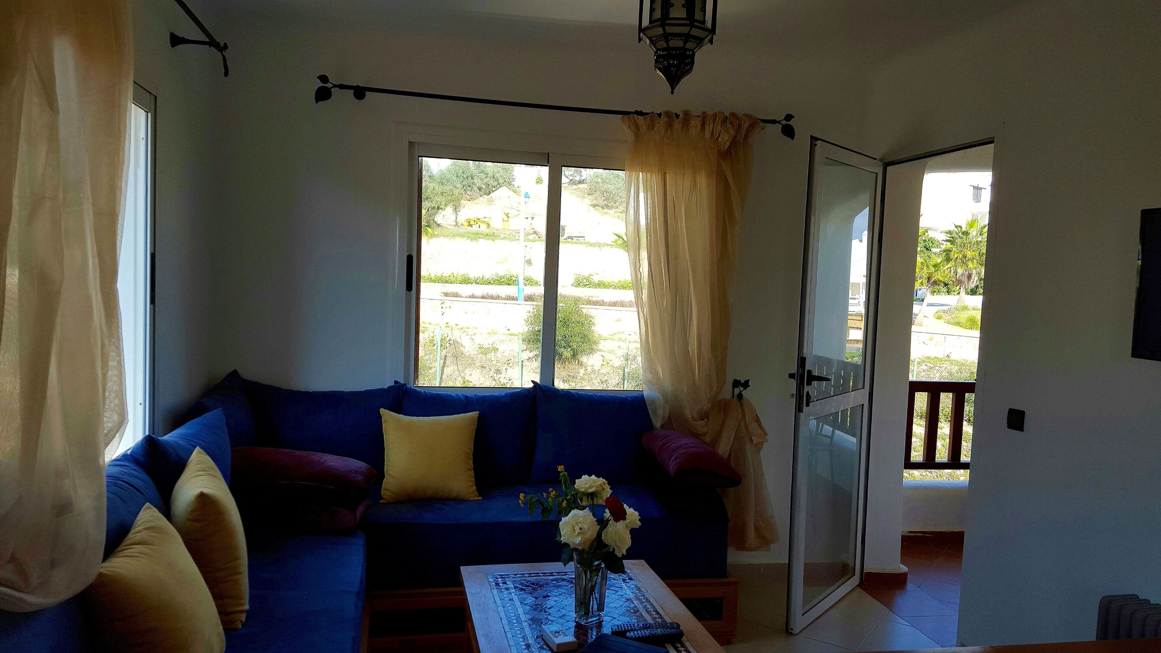 A living room with a blue sofa, a coffee table with a vase of flowers, and a view of the outside.