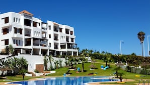 A hotel with a swimming pool, surrounded by greenery and palm trees.