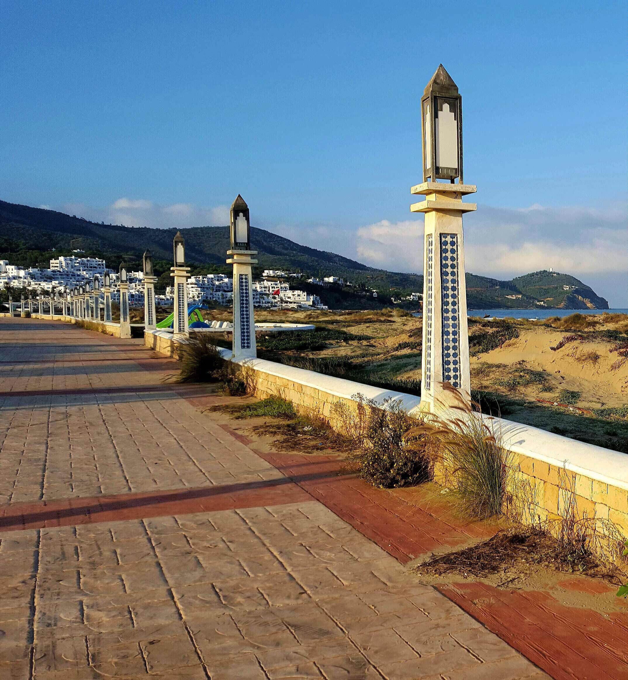 A coastal walkway with lamp posts and a paved path leading to a beach.